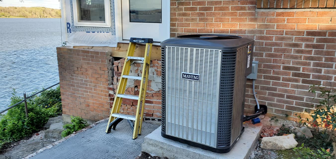 A new condenser and electrical disconnect sit beside a brick wall near a lake in South Pittsburg, TN — Kilgore Heating and Air
