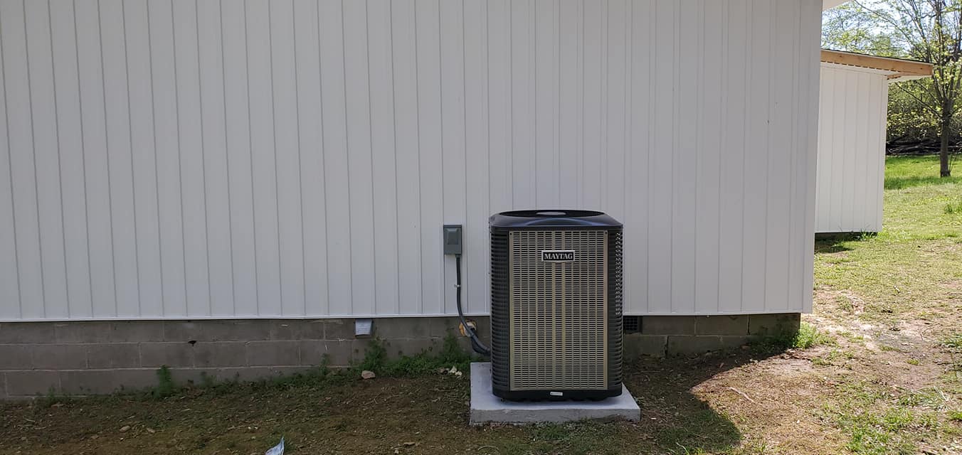A dark outdoor condenser sits on a pad against a light metal-sided home in Kimball, TN — Kilgore Heating and Air