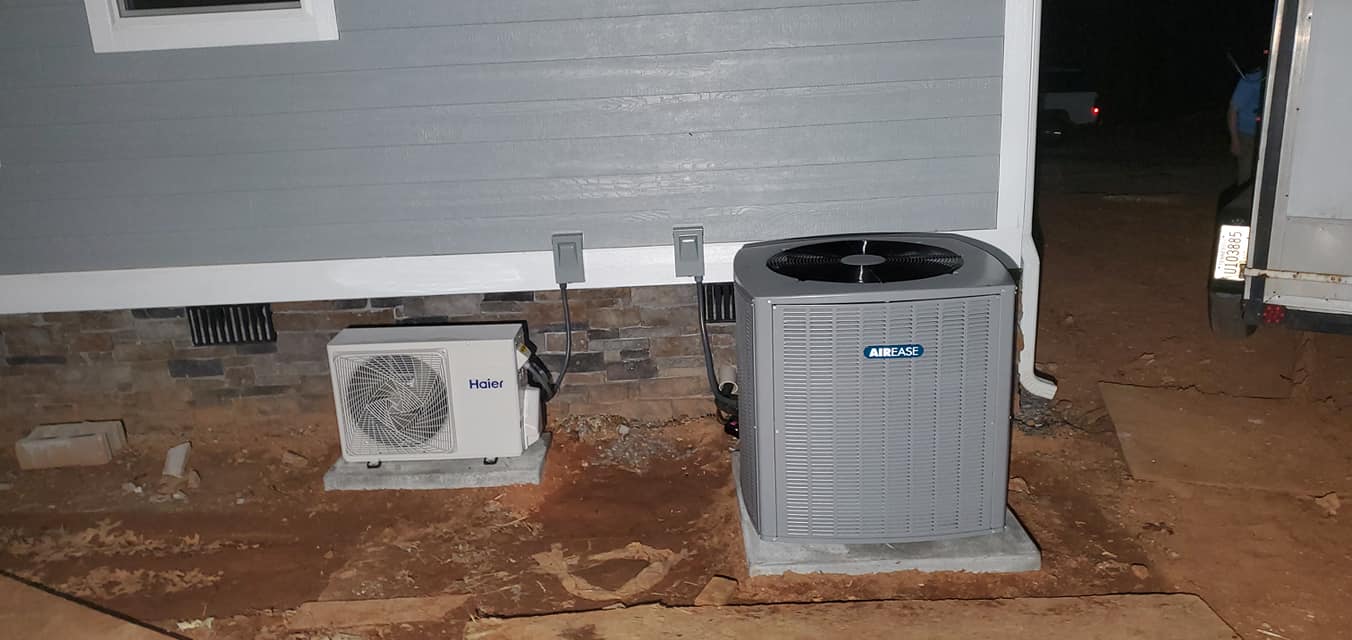 A central condenser and a smaller ductless outdoor unit sit beside a stone-faced home in Marion County, TN — Kilgore Heating and Air