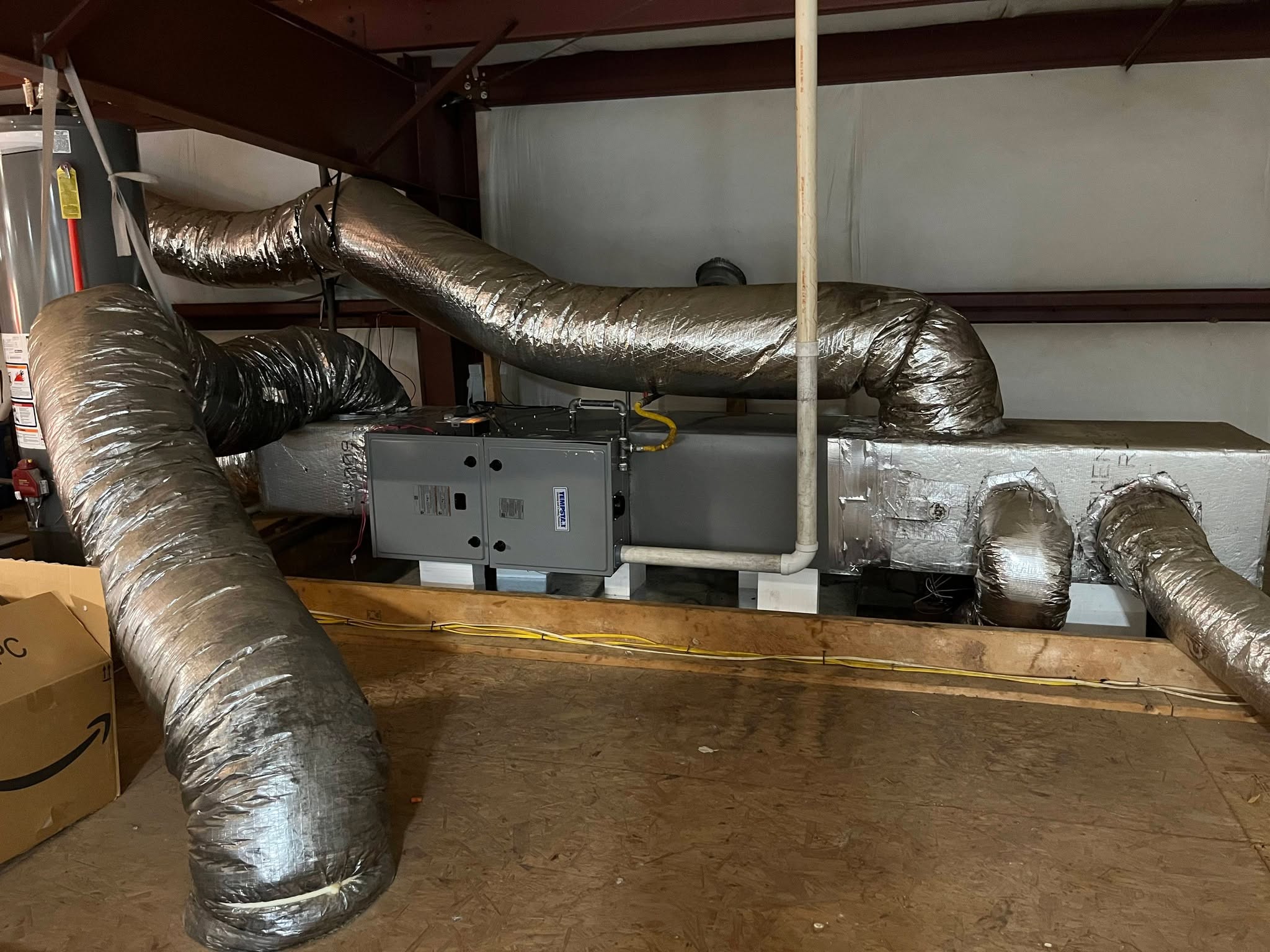 A horizontal indoor air handler connects to large reflective flex ducts in a mechanical area — diagnosing loud noises from an HVAC unit