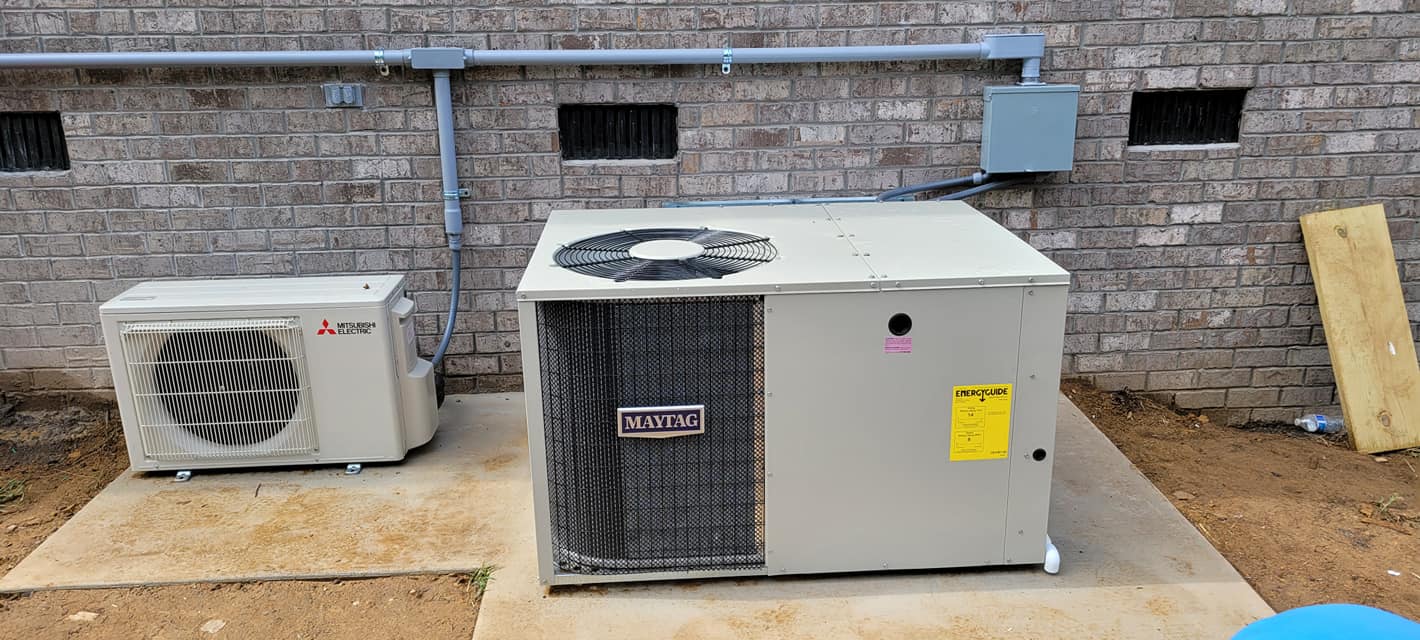 A Mitsubishi ductless unit and central condenser sit together beside a brick foundation — diagnosing a heat pump frozen outside