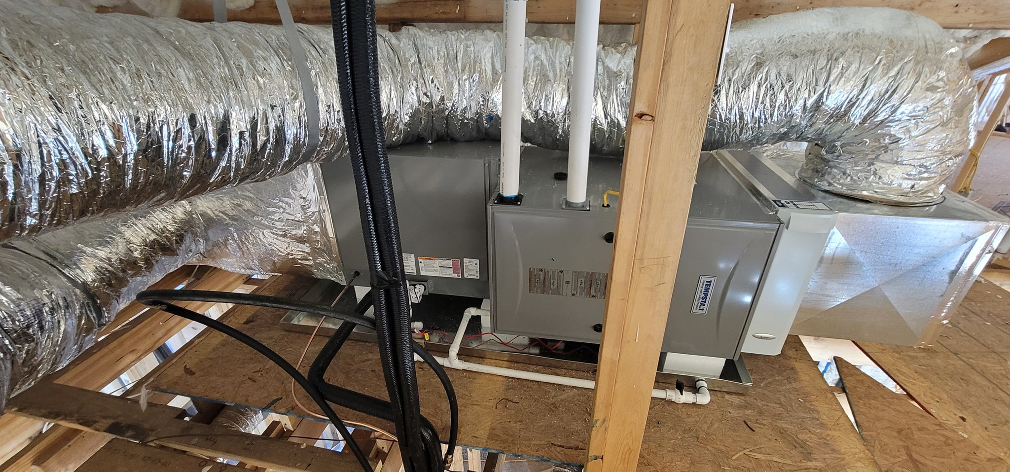 An air handler sits beneath a spray-foamed roof deck with flexible duct connections — foam-house HVAC when a previous contractor gave up