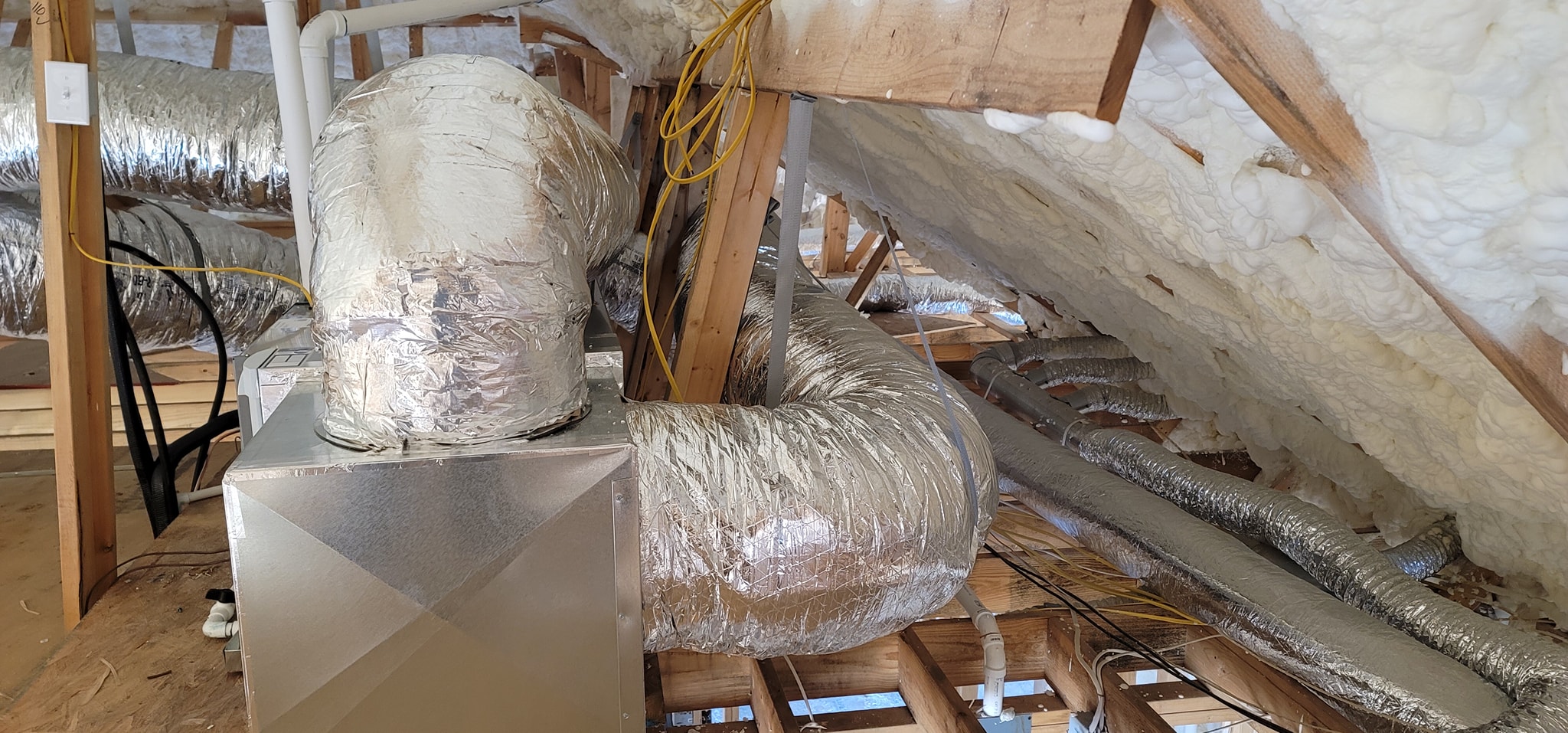 A compact air handler and insulated ducts are installed beneath a spray-foamed roof deck — right-sizing HVAC for a foam-insulated house
