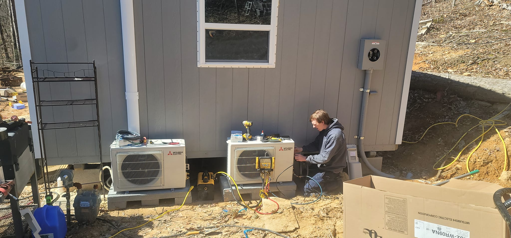 A technician works beside outdoor mini-split condensers at a home under construction in the Kilgore HVAC service area by Kilgore Heating and Air
