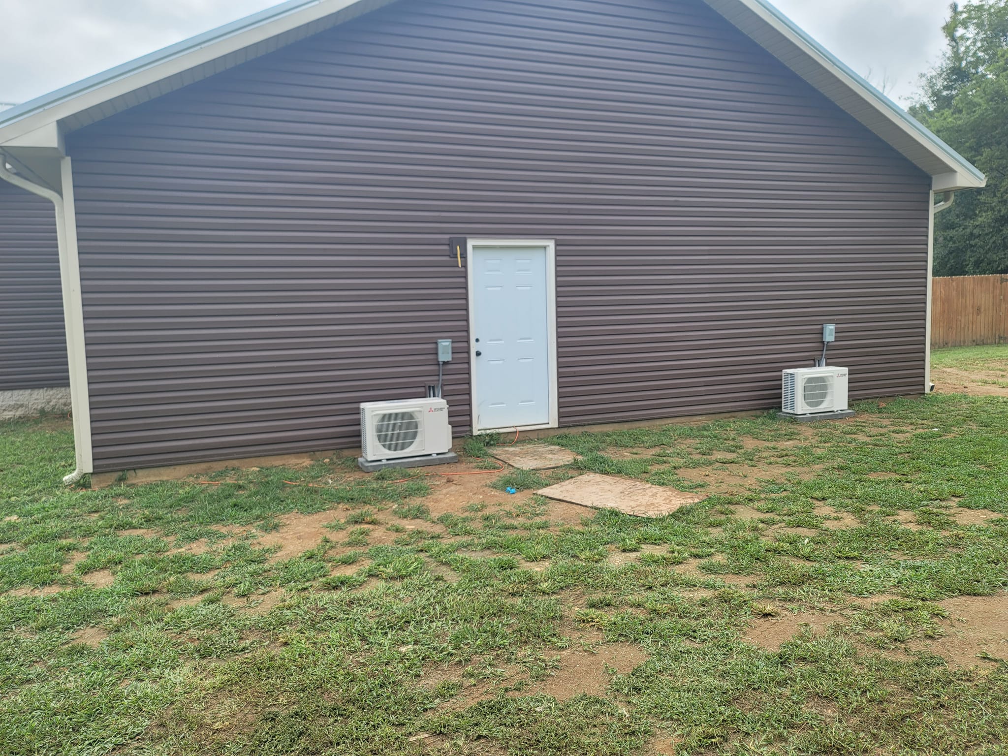 Two small outdoor mini-split condensers are installed along the side of a finished building — diagnosing an AC blowing warm air