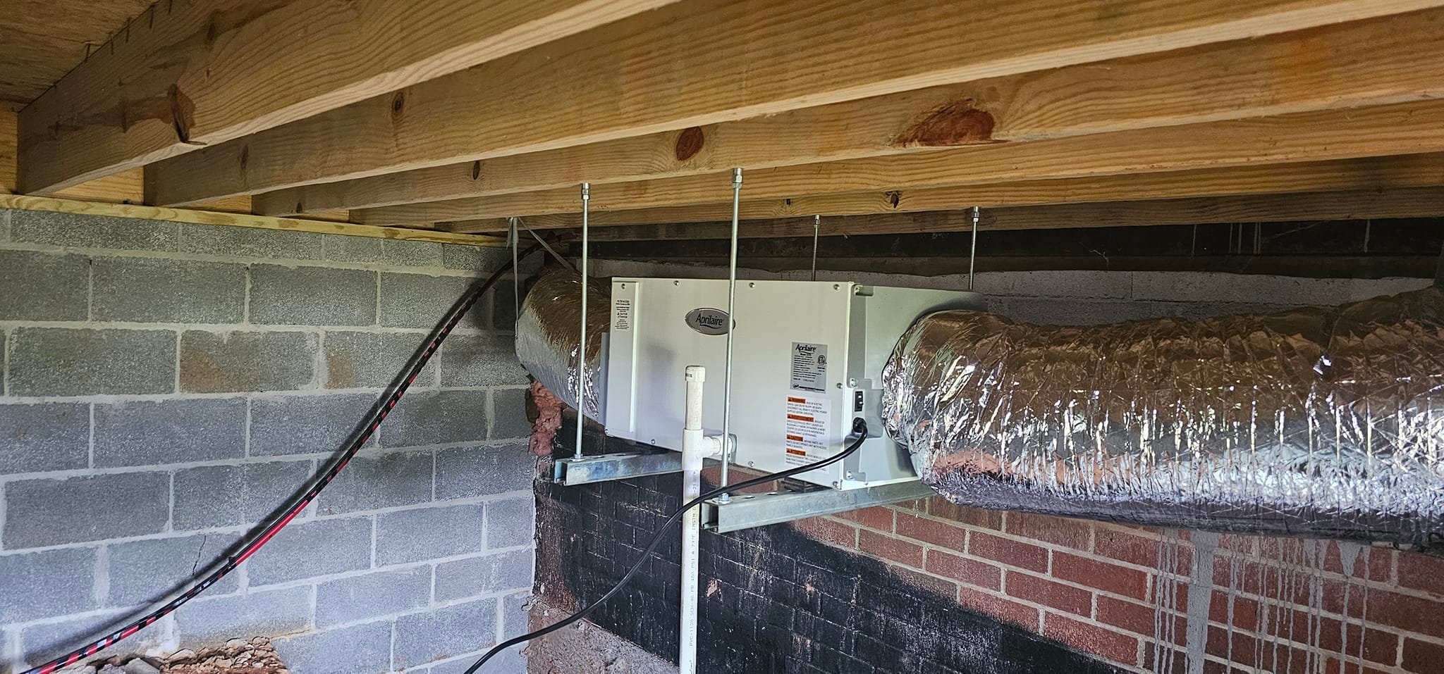 An air handler and insulated ductwork are installed in a low crawlspace beside a brick foundation — diagnosing humidity in a foam-insulated house