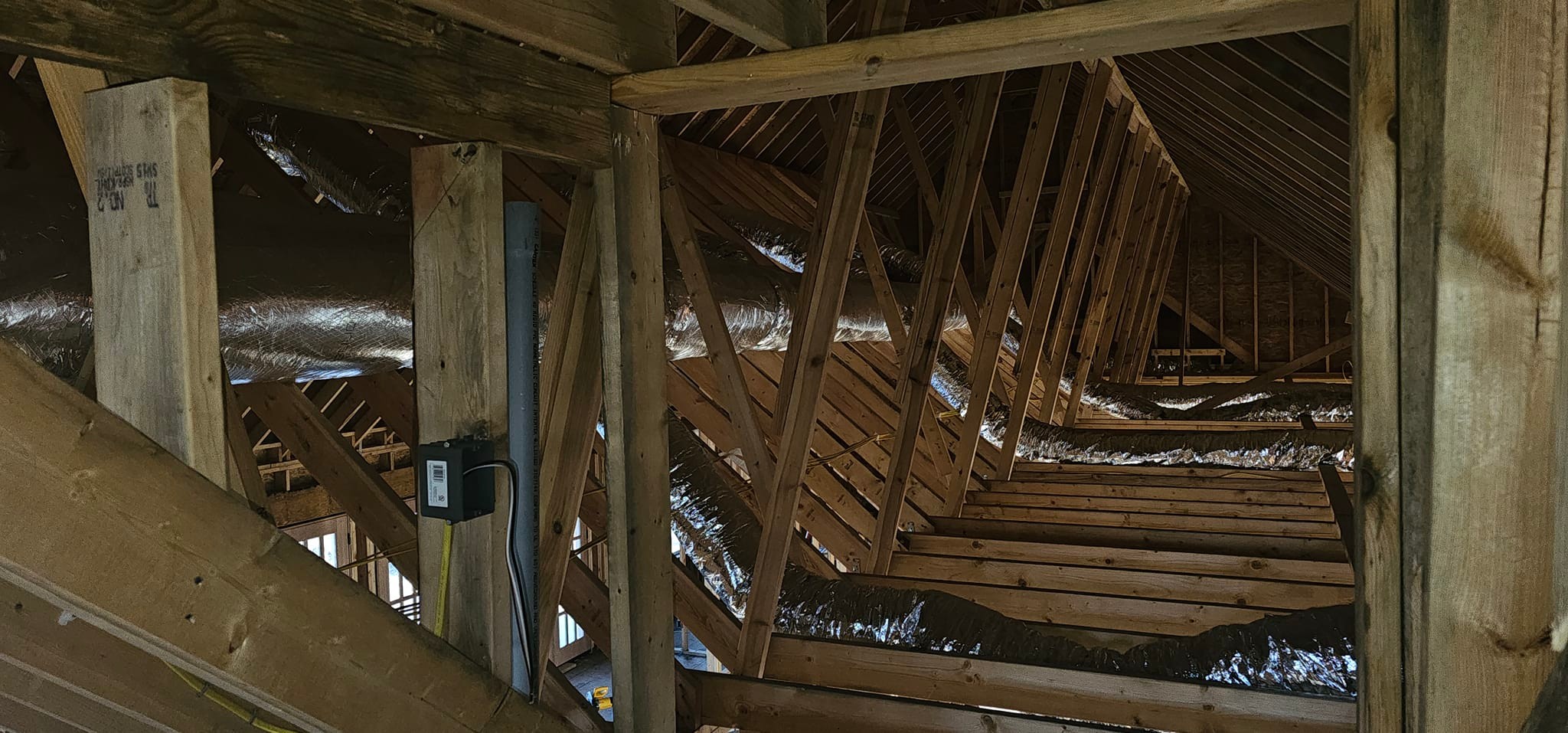 Reflective ductwork is routed through a framed attic beside a small indoor unit — diagnosing musty smells from HVAC vents