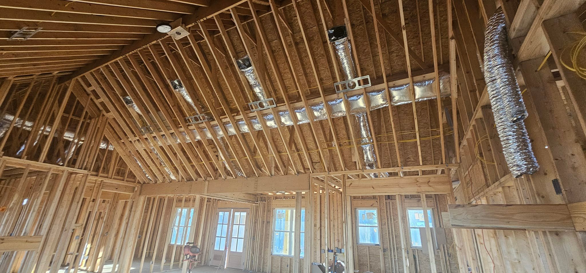 Reflective duct runs and ceiling boxes are installed across high open roof framing — diagnosing uneven cooling in a two-story home